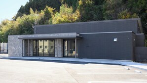 A modern building with a flat roof, large glass windows, and a stone facade. - Ties Verde Hotel (Okuma)