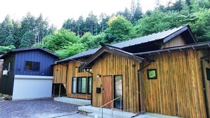 A row of wooden cabins with a gravel driveway and a forested hillside in the background. - Totonoi Kominka Villa Igashima (Aga)