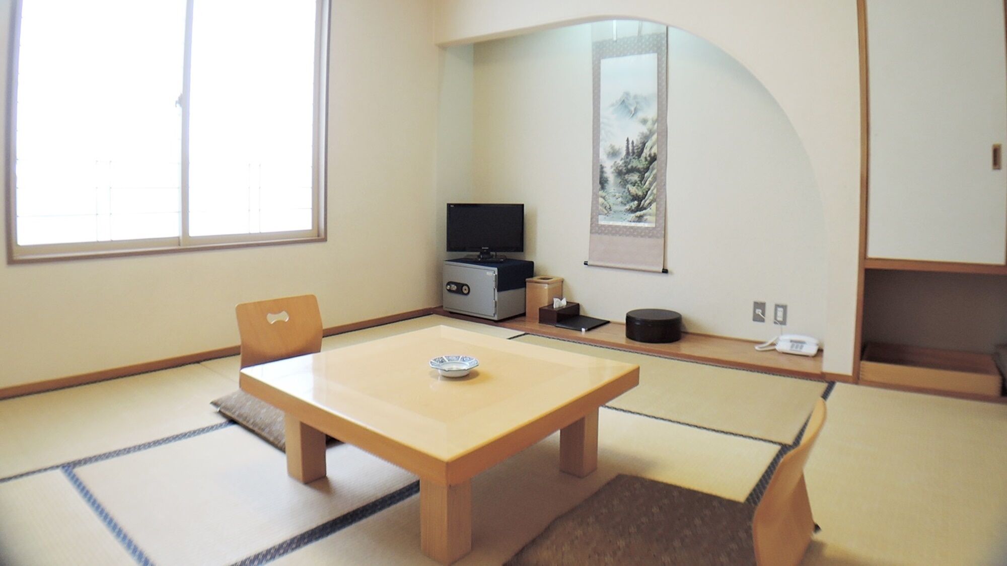 Una habitación de estilo japonés tradicional con suelo de tatami, una mesa baja, un televisor y una obra de arte enmarcada en la pared.