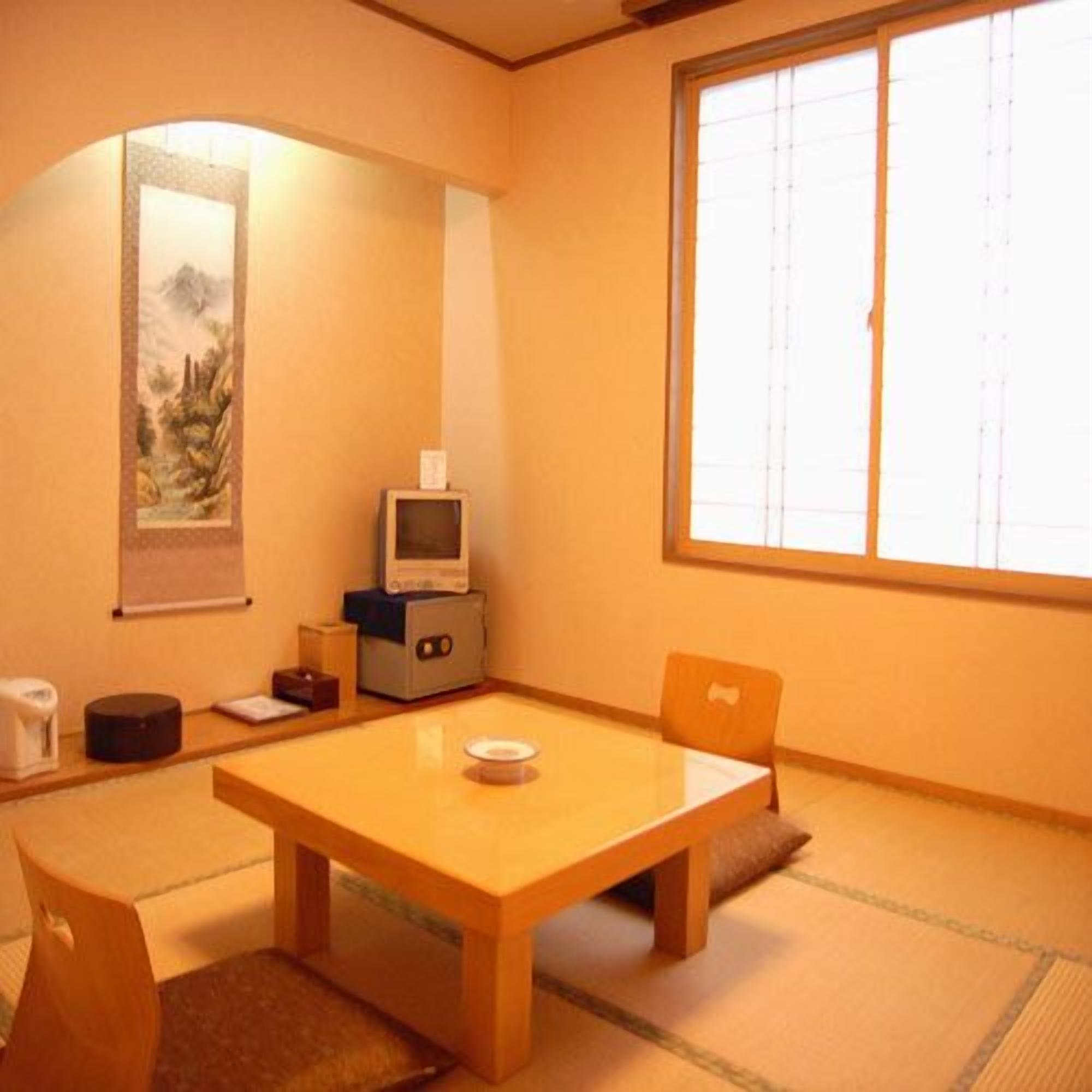 Una habitación japonesa tradicional con suelo de tatami, una mesa baja, un televisor y un panel shoji.