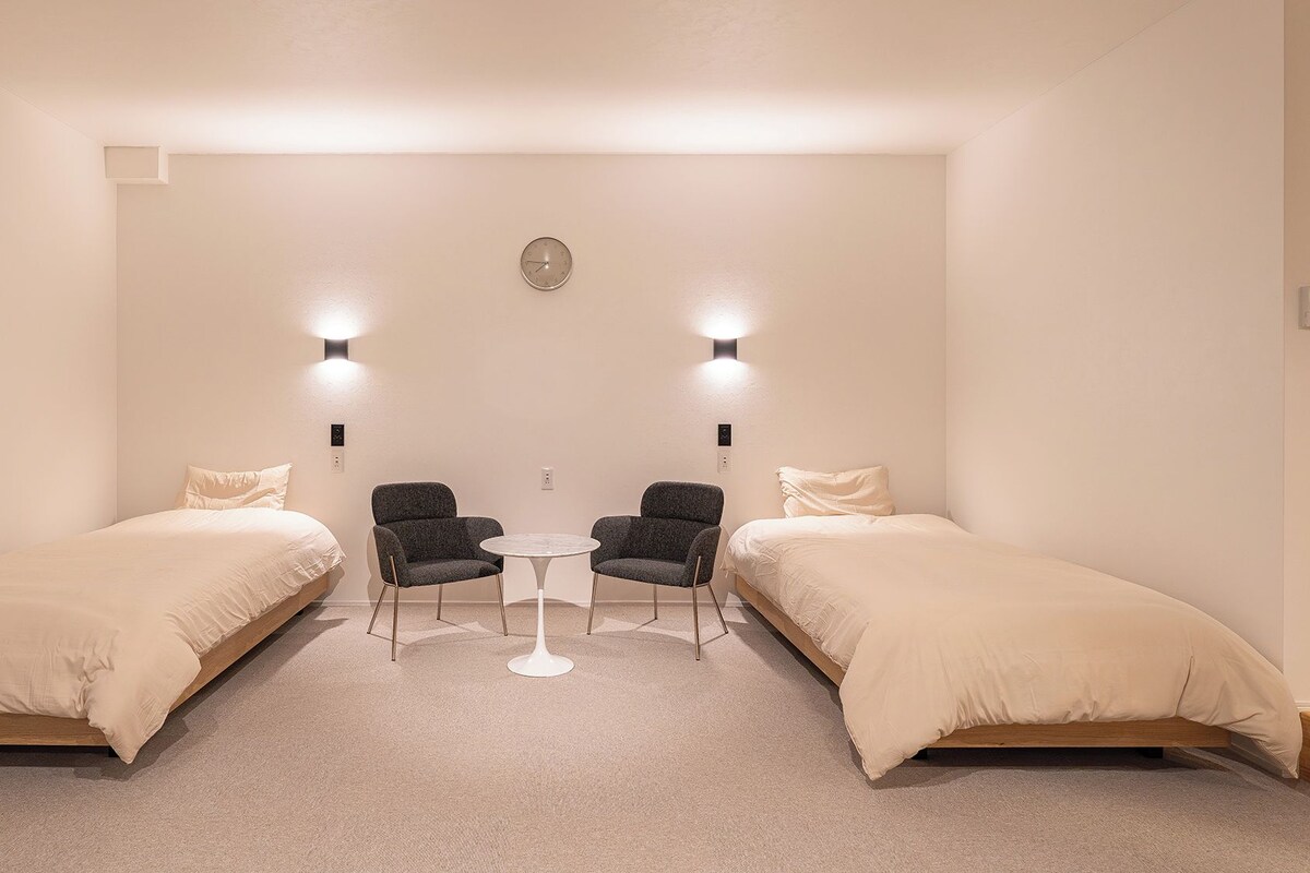 Une chambre avec deux lits, une petite table, deux chaises et des lampes fixées au mur.