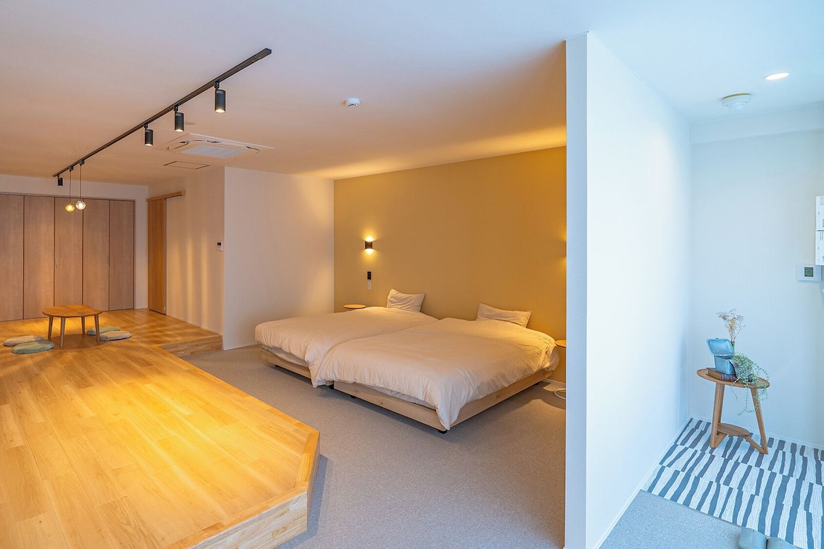 Ein modernes Hotelzimmer mit Holzboden, einem großen Bett, einem Schreibtisch und einem kleinen Tisch mit einer Pflanze.