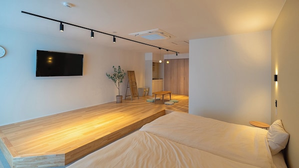 A modern bedroom with a wooden platform bed, a flat-screen TV, a potted plant, and a small table. - Renovation Hotel Gobo (Gobo)