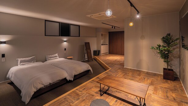A modern bedroom with a large bed, a wooden table, and a potted plant. - Renovation Hotel Gobo (Gobo)