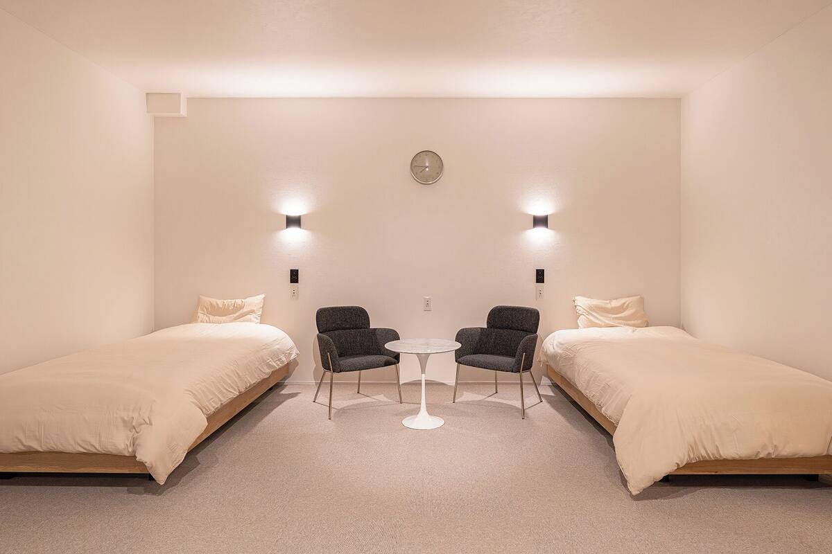Ein Schlafzimmer mit zwei Betten, einem kleinen Tisch, zwei Stühlen und Wandleuchten.