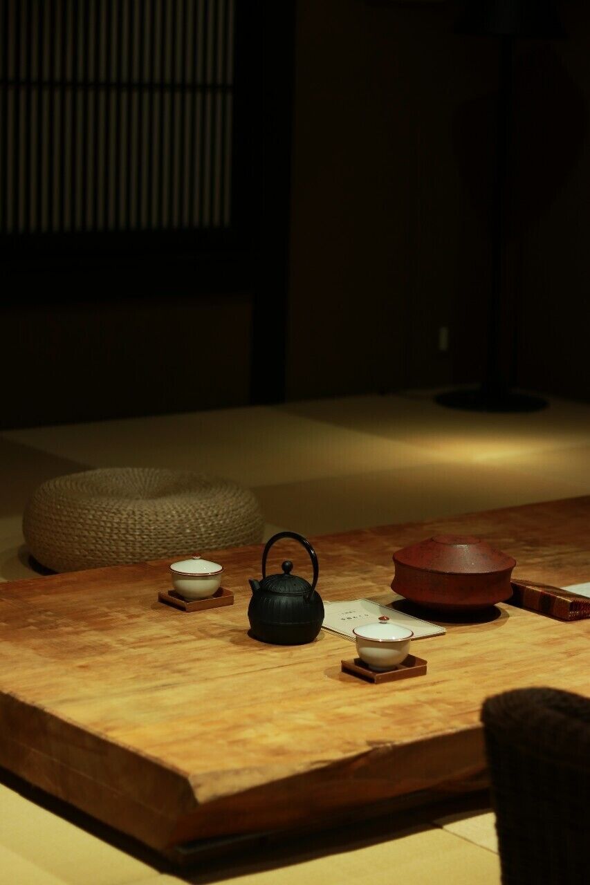 Una habitación japonesa tradicional con suelo de tatami, una mesita baja con utensilios para té y un taburete tejido.