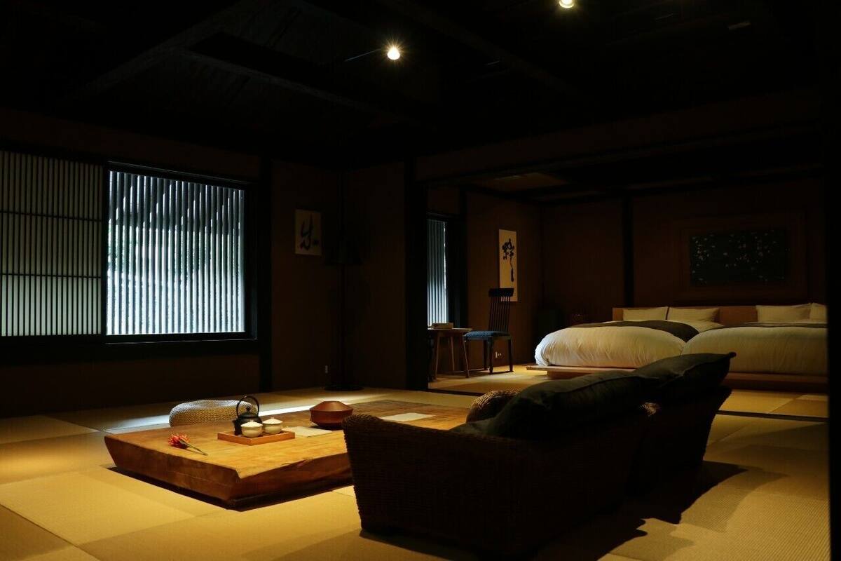 Perinteinen japanilaistyylinen huone, jossa on tatamimatto, matala pöytä teekupit ja -tarvikkeineen, tyynyillä varustettu sänky ja liukuvat ovet.