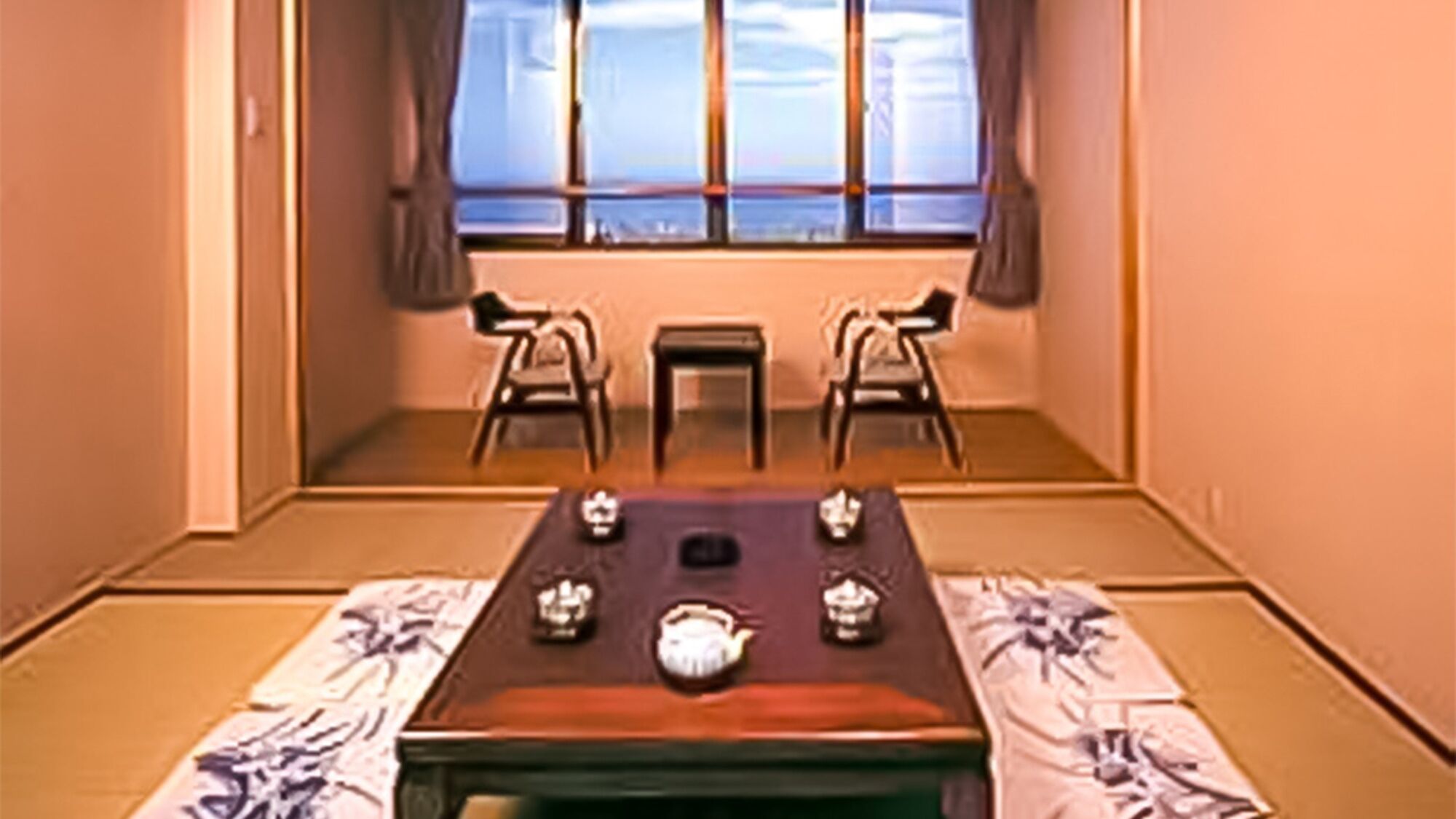 A traditional Japanese room with tatami flooring, a low table with a tea set, and two chairs.