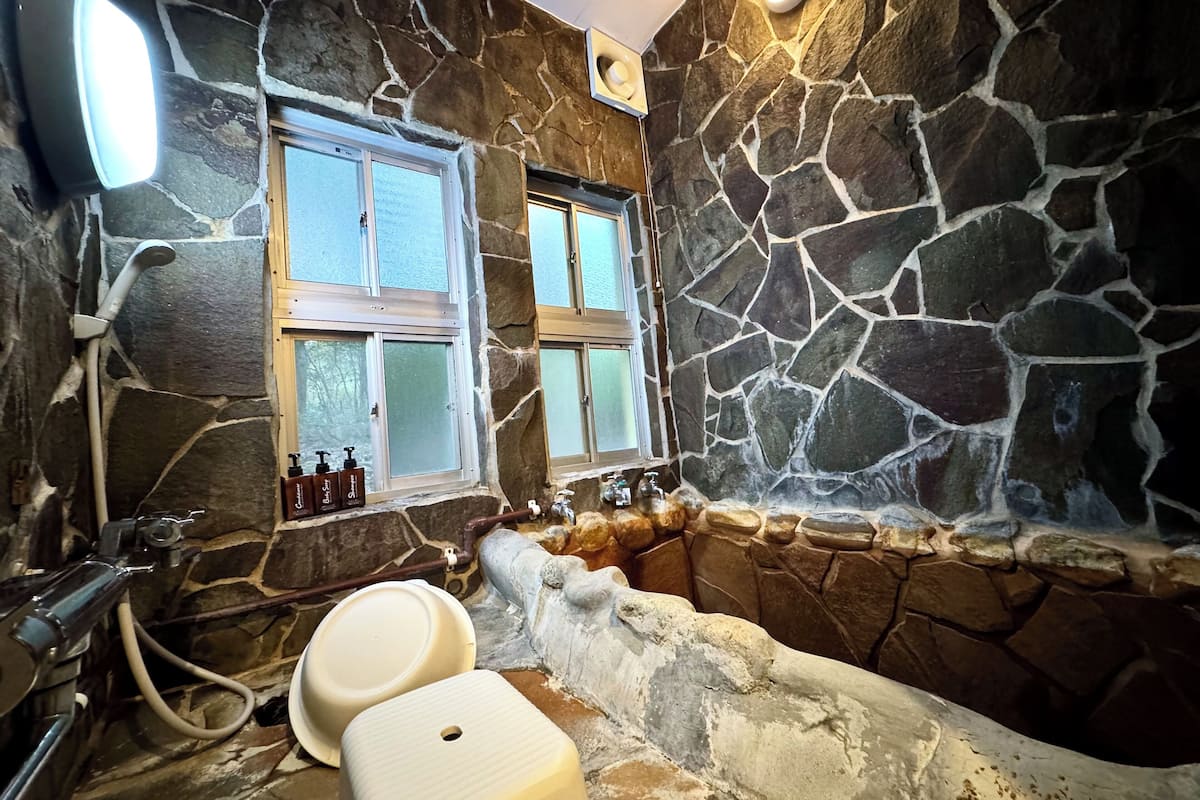A bathroom with stone walls, a bathtub, a sink, and two windows.