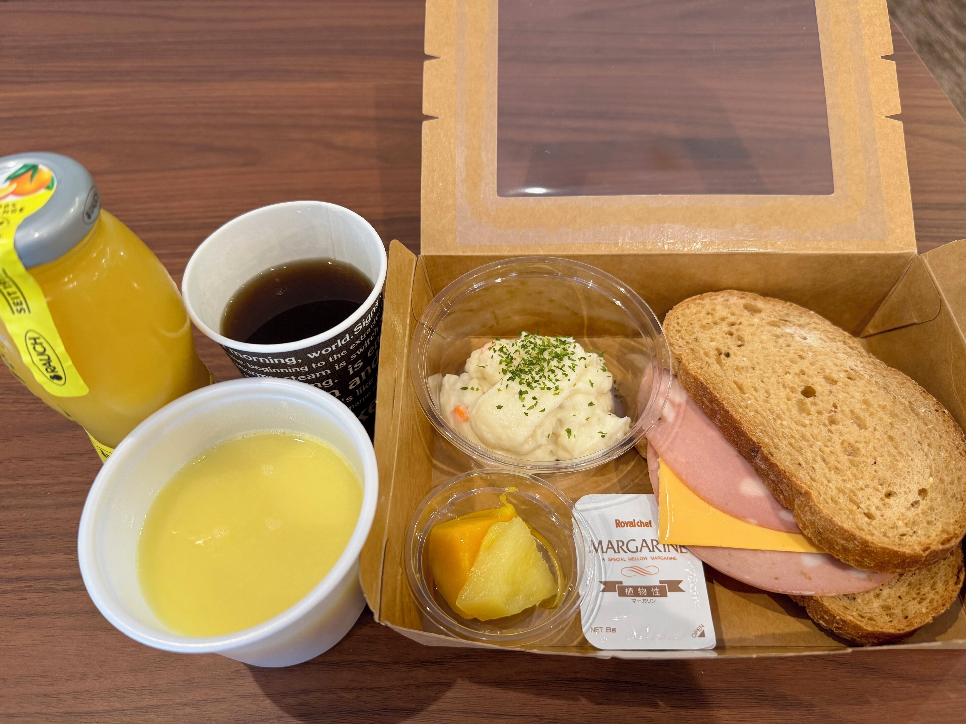Eine Mahlzeit mit Brot, Schinken, Käse, Beilagen, einer Tasse Kaffee und einer Saftflasche.