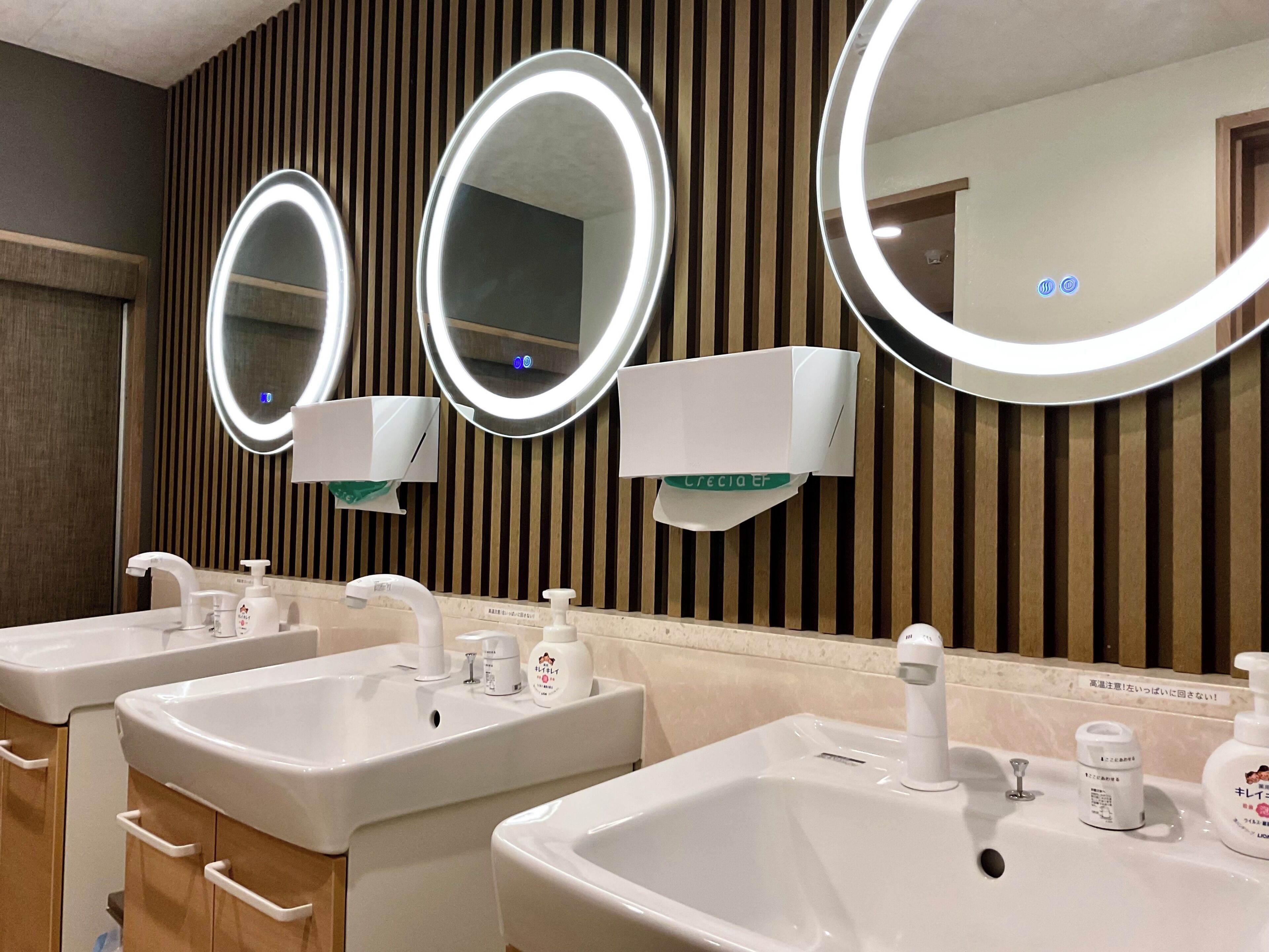 A bathroom with three sinks, each with a mirror and soap dispenser.