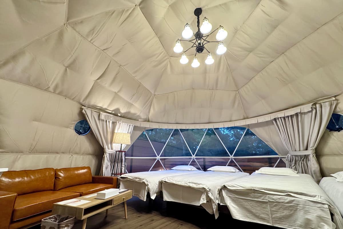 A tented accommodation with a bed, a sofa, a lamp, and a trash bin.