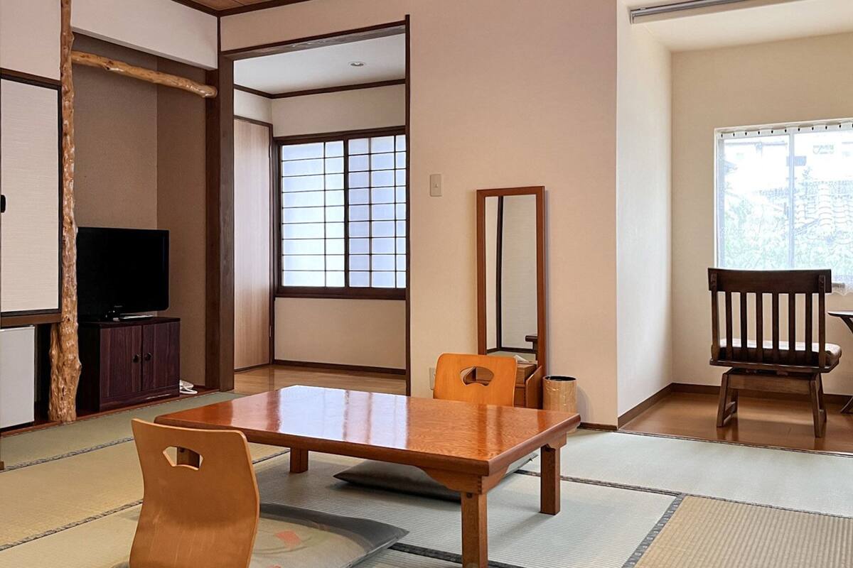 Une pièce de style japonais traditionnel, avec un sol recouvert de tatamis, une table basse, des chaises, un téléviseur et une porte coulissante.