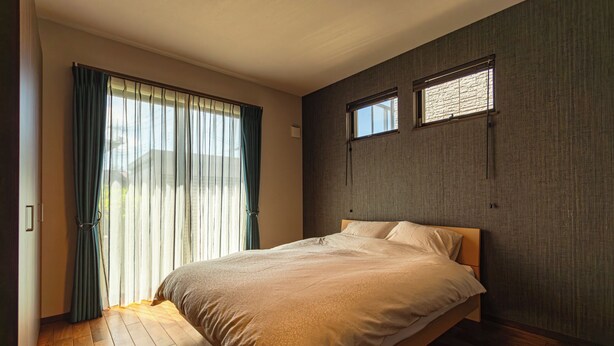 Une chambre à coucher avec un lit, un plancher en bois, une fenêtre avec des stores et un mur à texture.