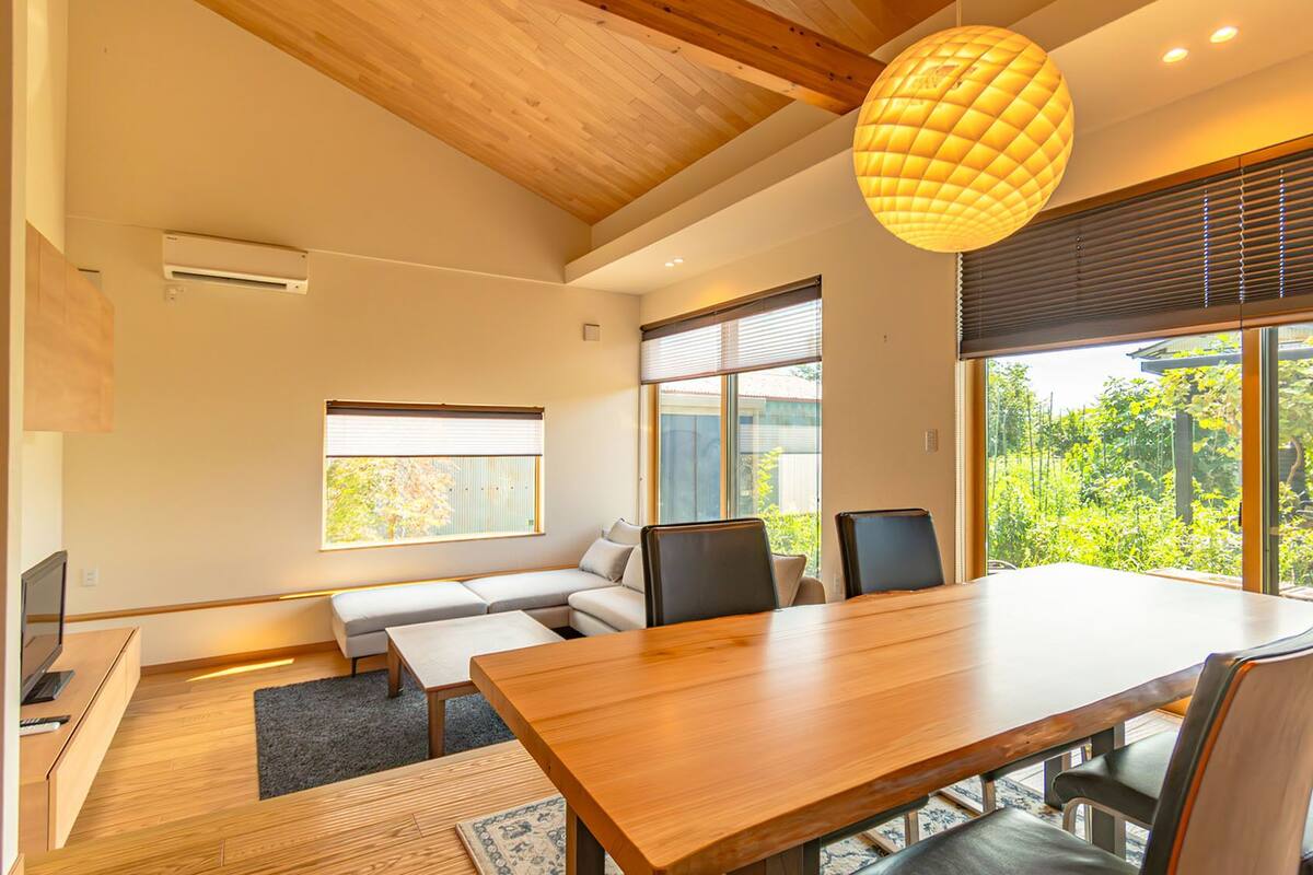 Un intérieur moderne avec une table à manger en bois, des chaises, un canapé et une grande fenêtre équipée de stores.