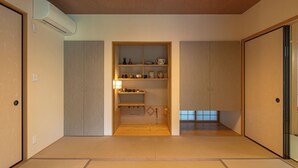 Une pièce de style japonais traditionnel, avec un sol recouvert de tatamis, une étagère intégrée où sont rangés divers objets et des portes coulissantes.