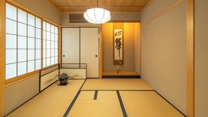Une pièce de style japonais traditionnel, avec un sol recouvert de tatamis, des portes coulissantes, un paravent shoji, un luminaire suspendu et une œuvre calligraphique accrochée au mur.