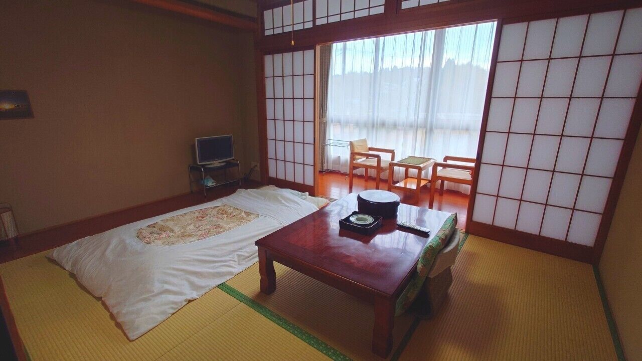 Una habitación japonesa tradicional con suelo de tatami, un futón, una mesa de madera con juego de té y puertas correderas shoji.