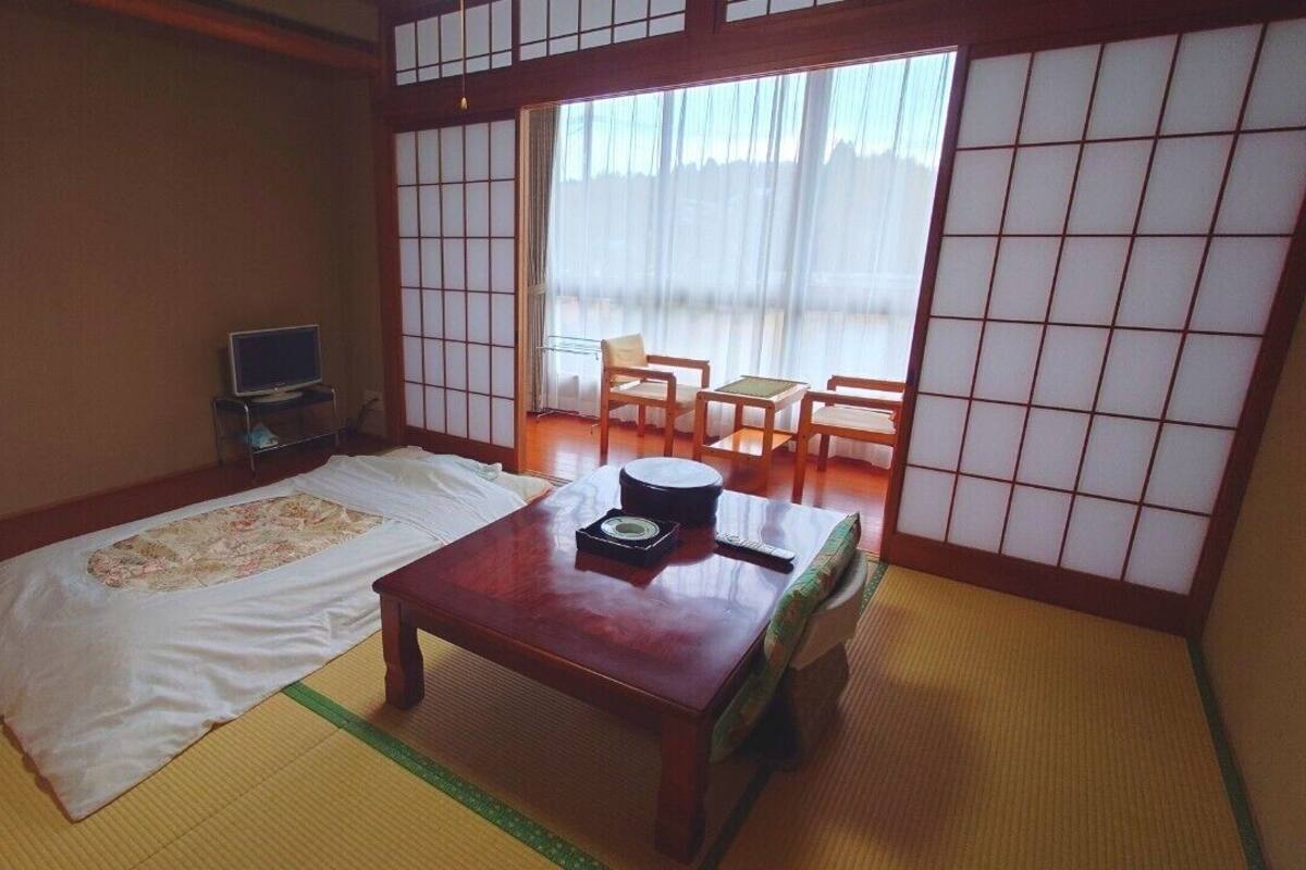 A traditional Japanese room with tatami flooring, a futon bed, a wooden table with a tea set, and sliding shoji doors.