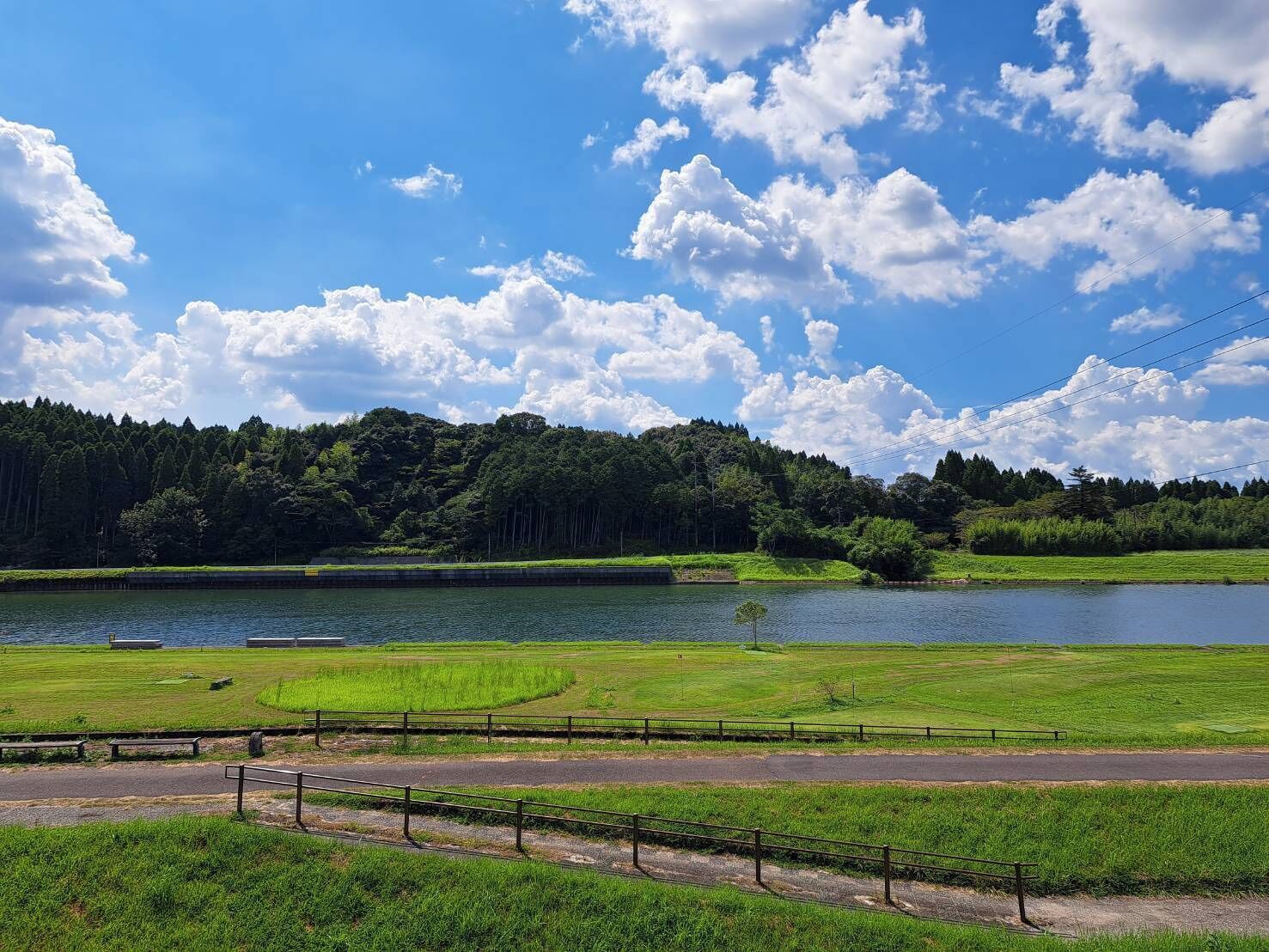 Un parque con un lago, zonas verdes y una carretera con valla.