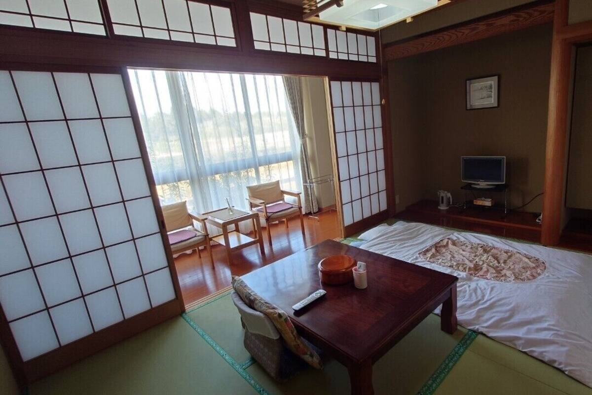 A traditional Japanese-style room with tatami flooring, a futon bed, a wooden table, a television, and sliding doors.