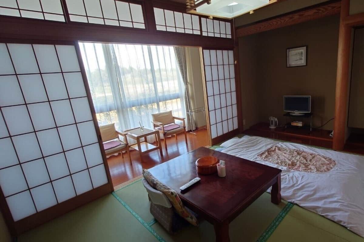Una habitación tradicional japonesa con suelo de tatami, futón, mesa de madera, televisor y puertas correderas.