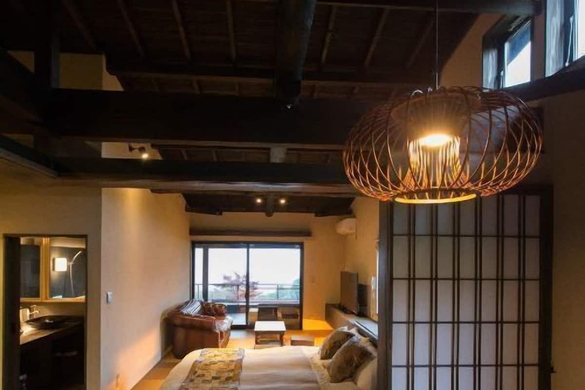 Une chambre à coucher comprenant un lit, un bureau, une chaise, un canapé, une fenêtre et une porte coulissante traditionnelle.