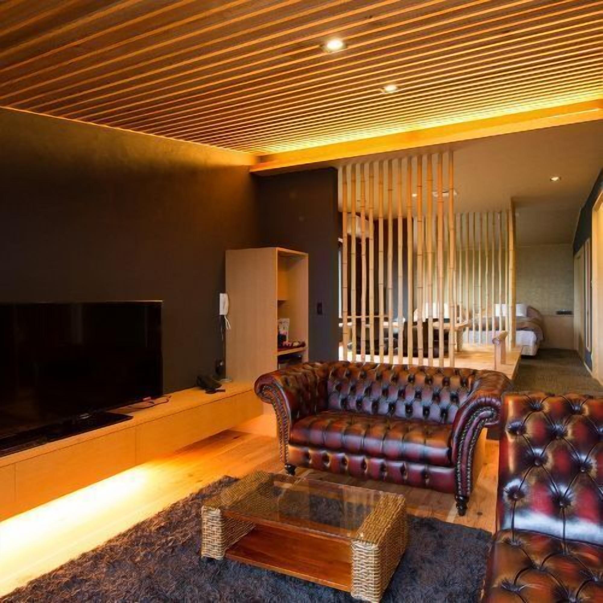 Una sala de estar moderna con un televisor de pantalla plana grande, sofás de cuero, una mesa de centro de vidrio y techo de madera.