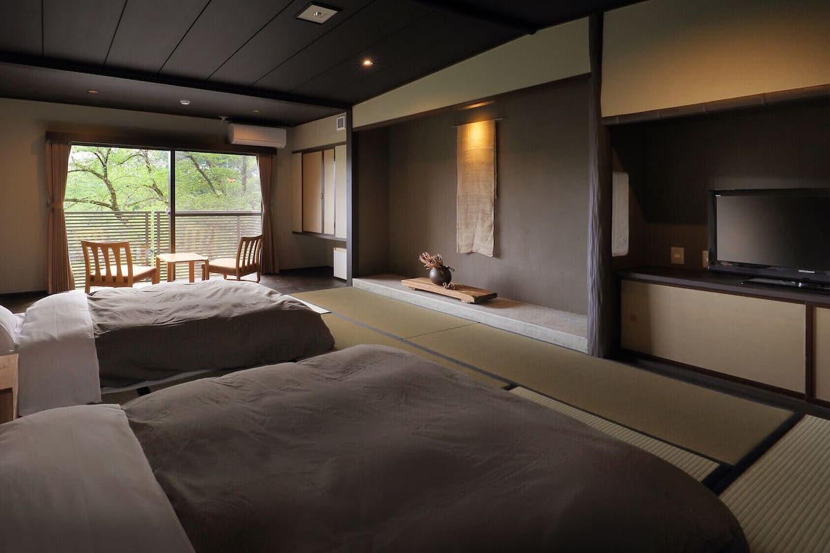 Habitación de hotel con dos camas, televisión, una mesita con un jarrón y vistas a zonas verdes.