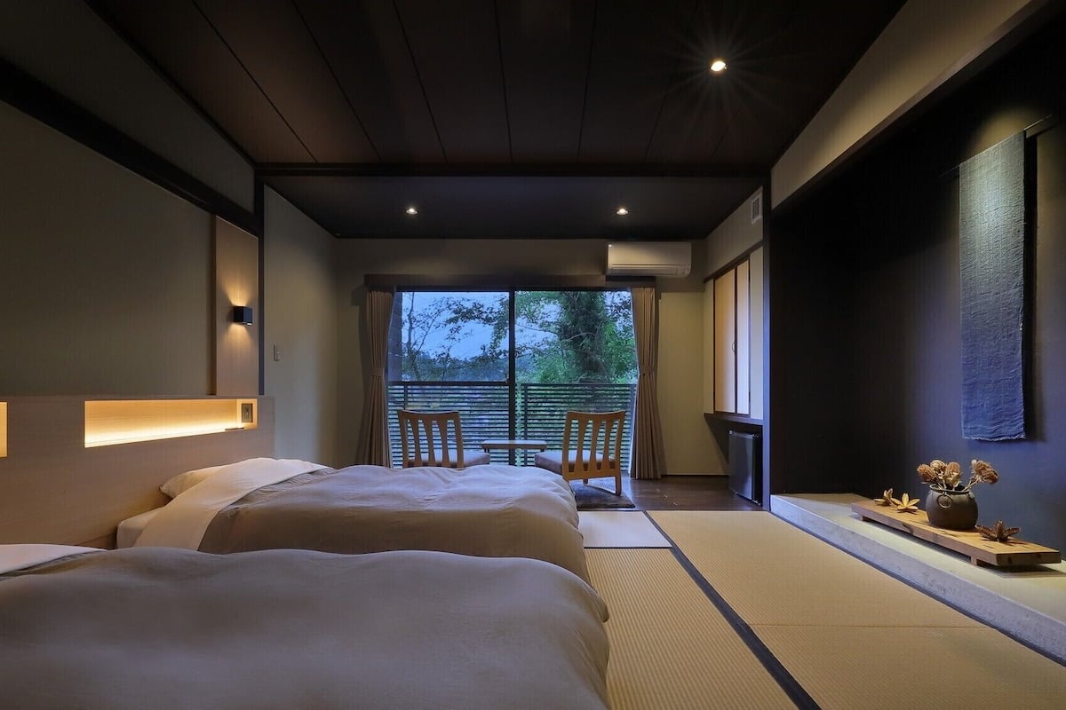 Habitación de hotel moderna con dos camas, una mesita, sillas, vistas al exterior y un jarrón decorativo.
