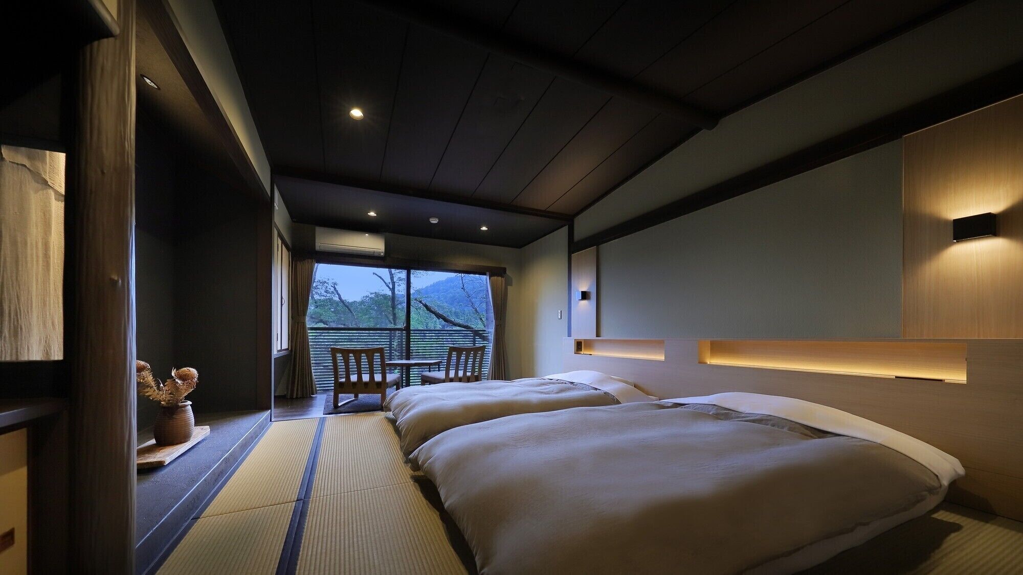 A hotel room with a bed, bedside table, and a view of the outdoors.