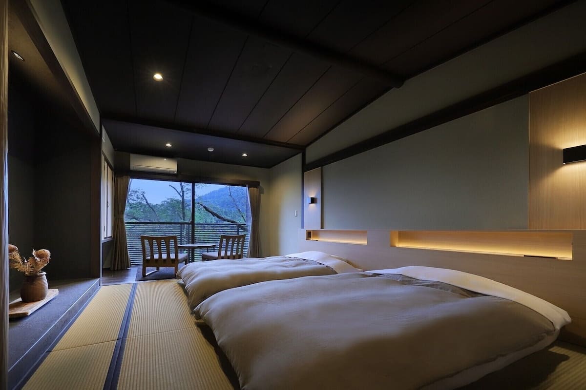 Una habitación de hotel con cama, mesita de noche y vistas al exterior.