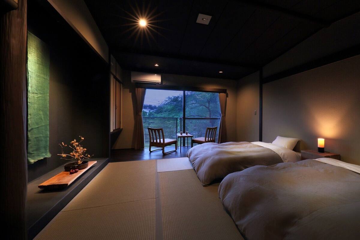 Habitación de hotel con dos camas, una mesita, una silla y vistas al exterior.