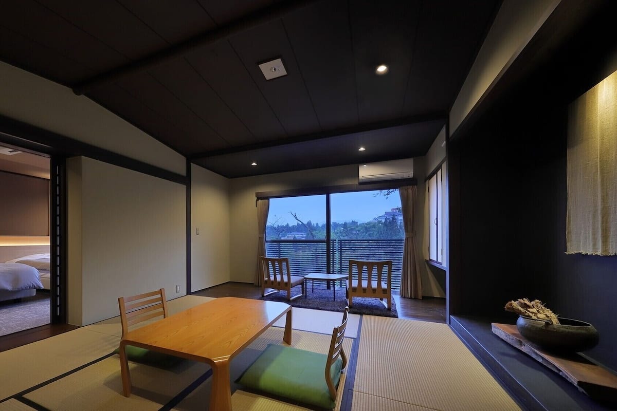 Una habitación tradicional japonesa con suelo de tatami, una mesa baja y vistas a un paisaje urbano.