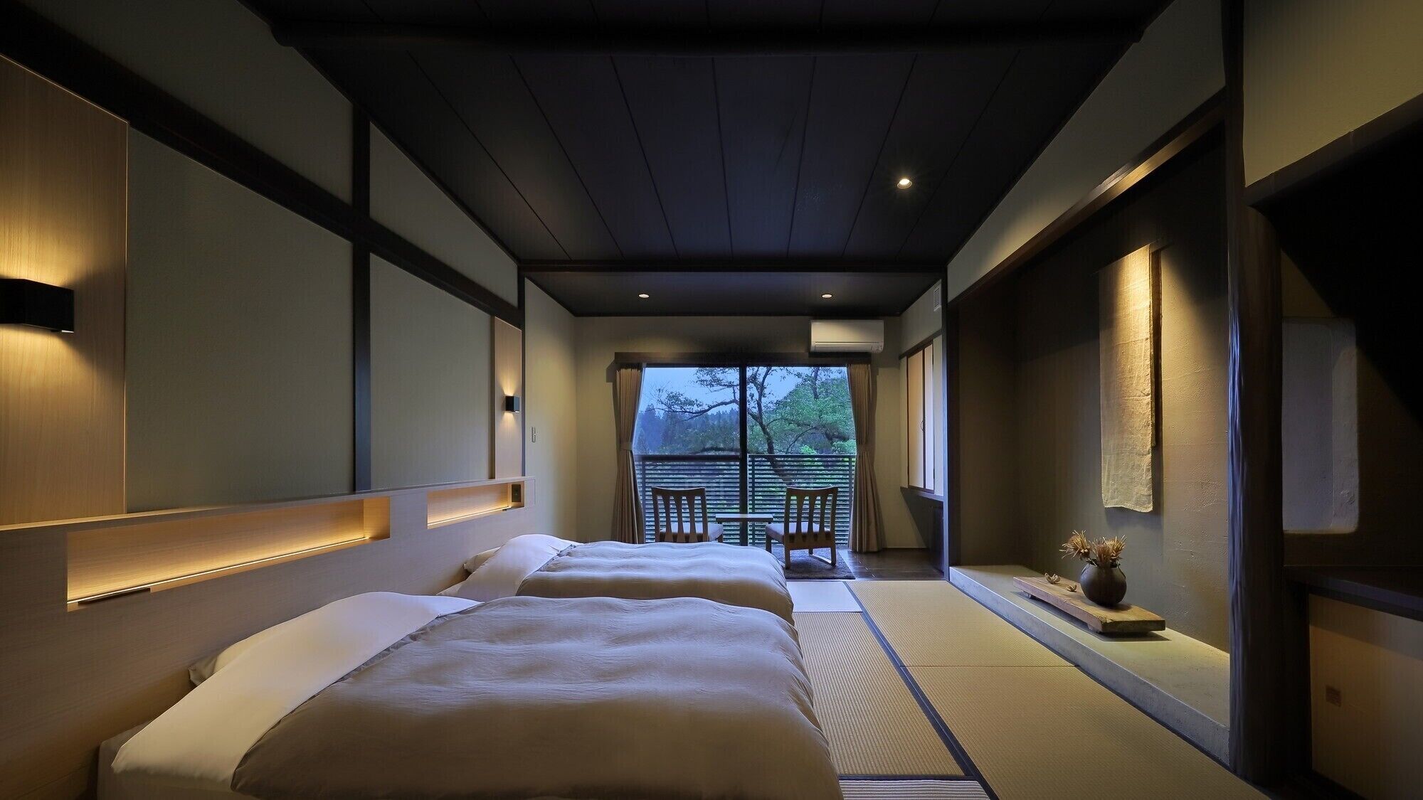 A hotel room with a traditional Japanese aesthetic, featuring tatami flooring, a sliding door leading to a balcony, and a bed with a headboard.