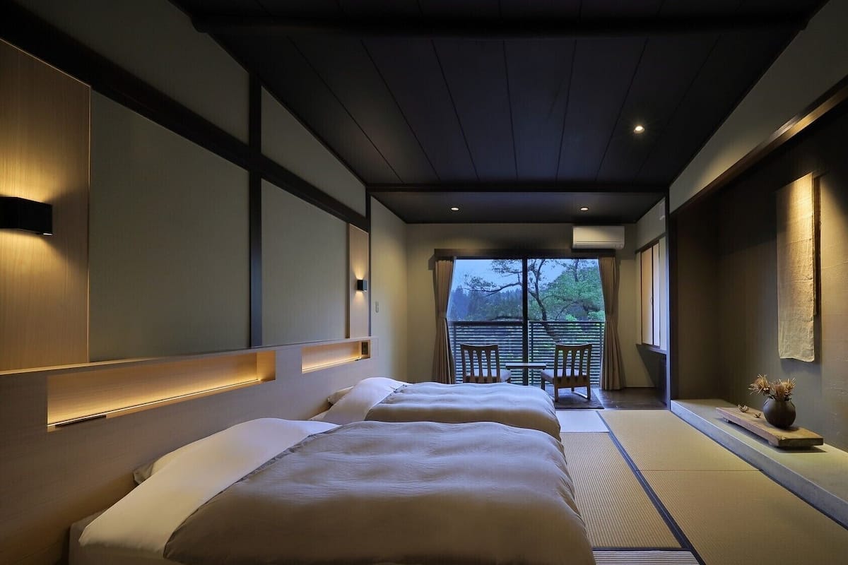 Habitación de hotel con estética japonesa tradicional, que presenta suelo de tatami, una puerta corredera que da a un balcón y una cama con cabecera.