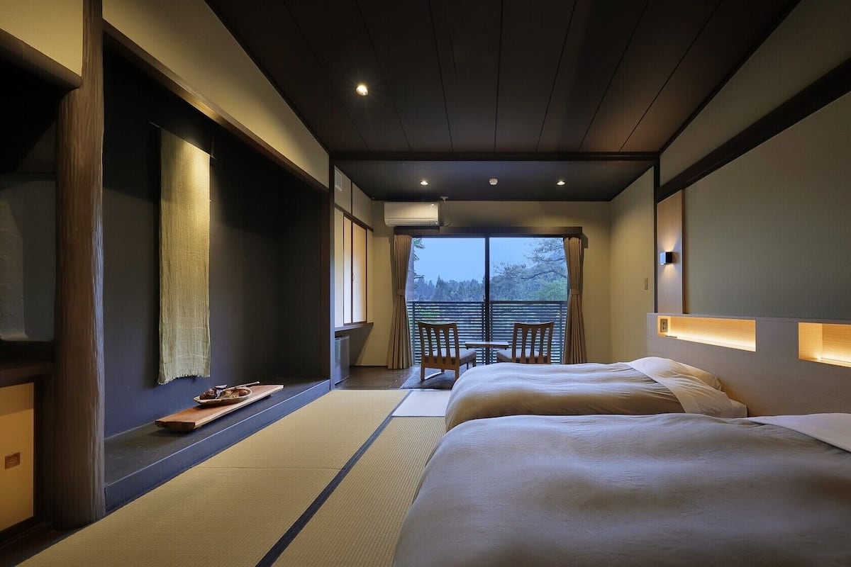 Habitación de hotel con cama, una mesita, sillas, vista a árboles y una puerta corredera.