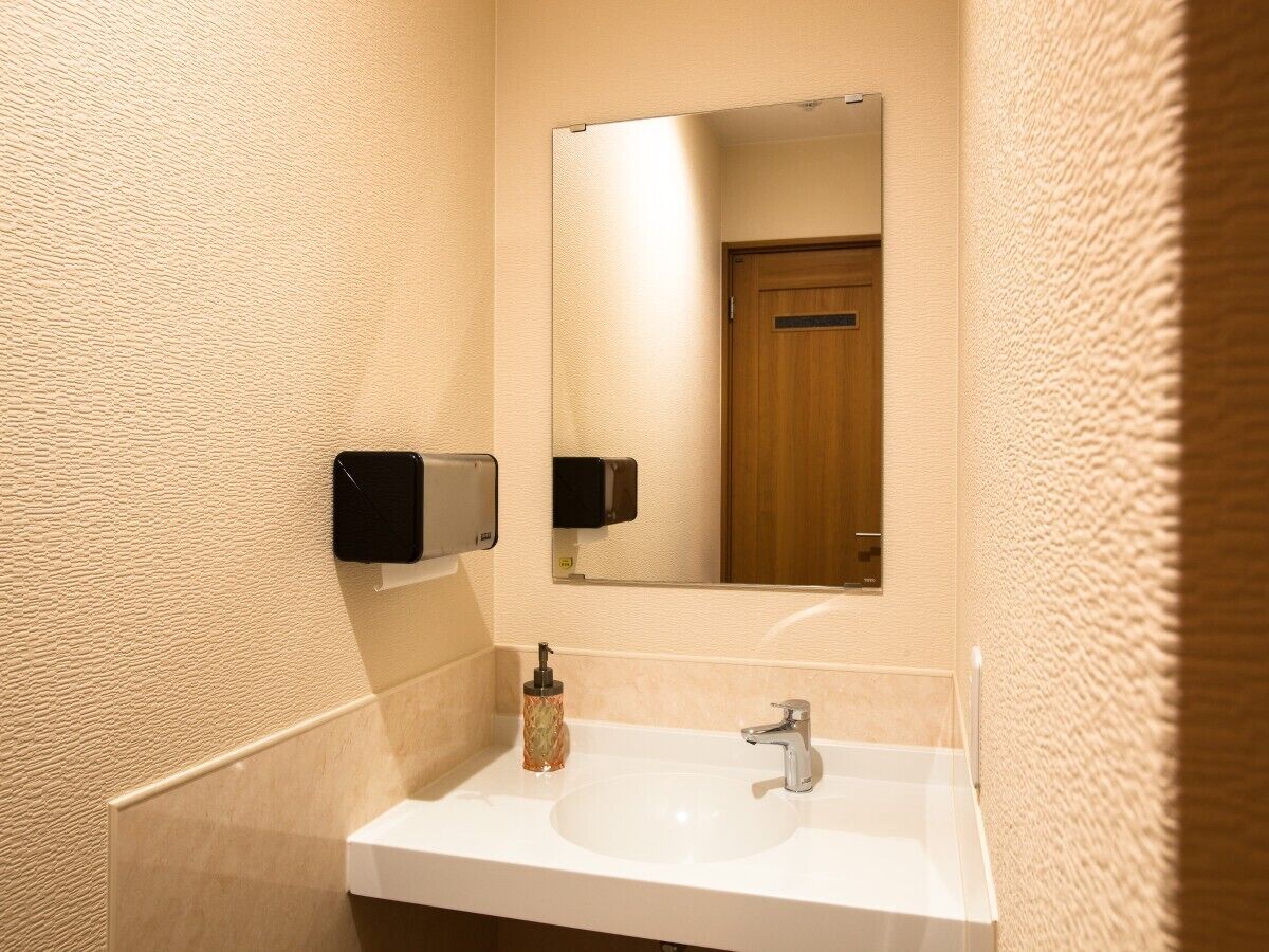 Une salle de bain avec un lavabo blanc, un miroir, un distributeur de savon et un distributeur de serviettes.