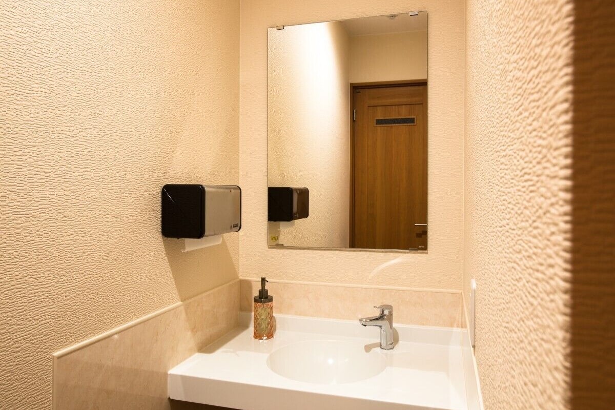 Ein Badezimmer mit einem weißen Waschbecken, einem Spiegel, einem Seifenspender und einem Handtuchspender.