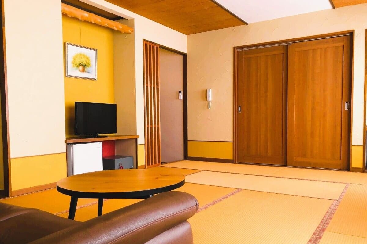 Ein Zimmer mit Tatami-Böden, einem Fernseher auf einer niedrigen Ablage, einer Holztür und einem Telefon an der Wand.