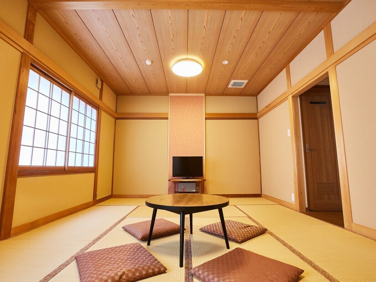 Une pièce de style japonais traditionnel, avec un sol recouvert de tatamis, une table basse en tatami, un téléviseur posé sur un meuble bas et une porte coulissante.