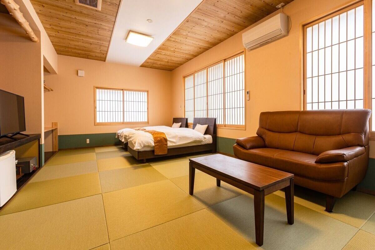 Ein Zimmer mit Tatami-Böden, einem Bett, einer Couch, einem Tisch und einem Fernseher.
