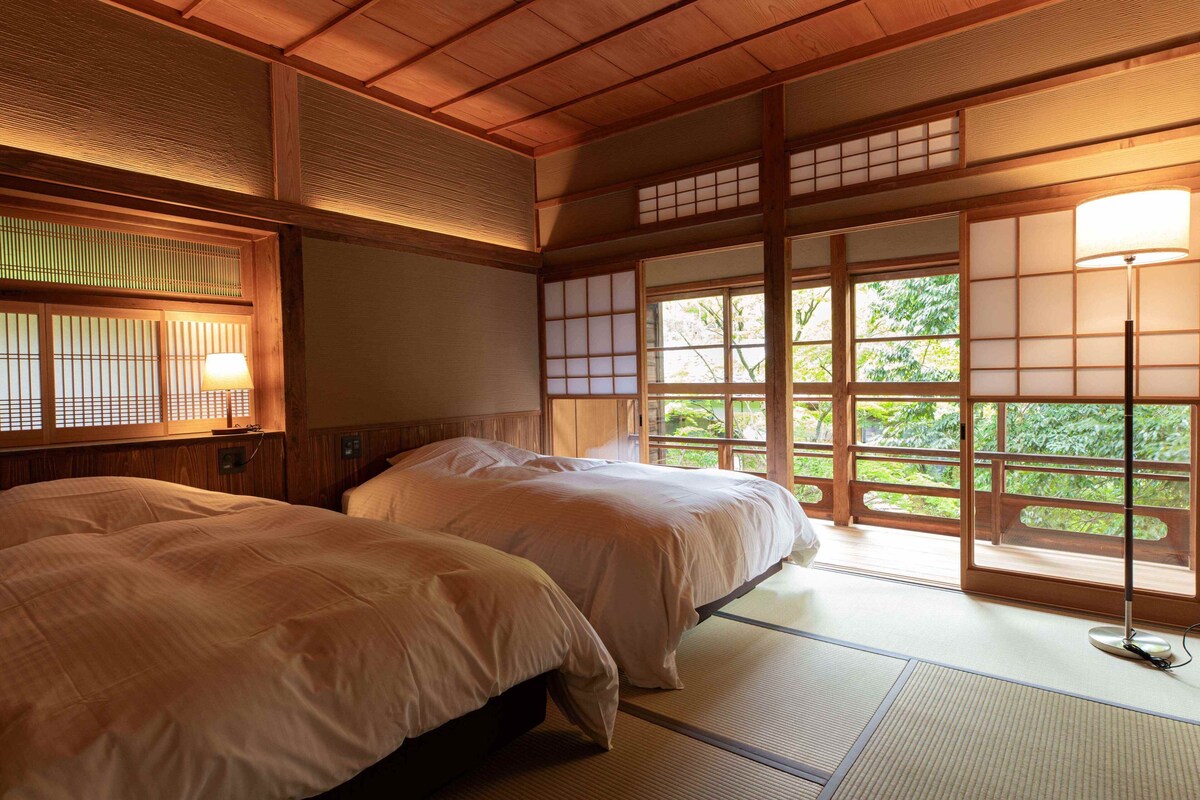 Um quarto japonês tradicional com tatames, duas camas, portas deslizantes e vista para o verde.