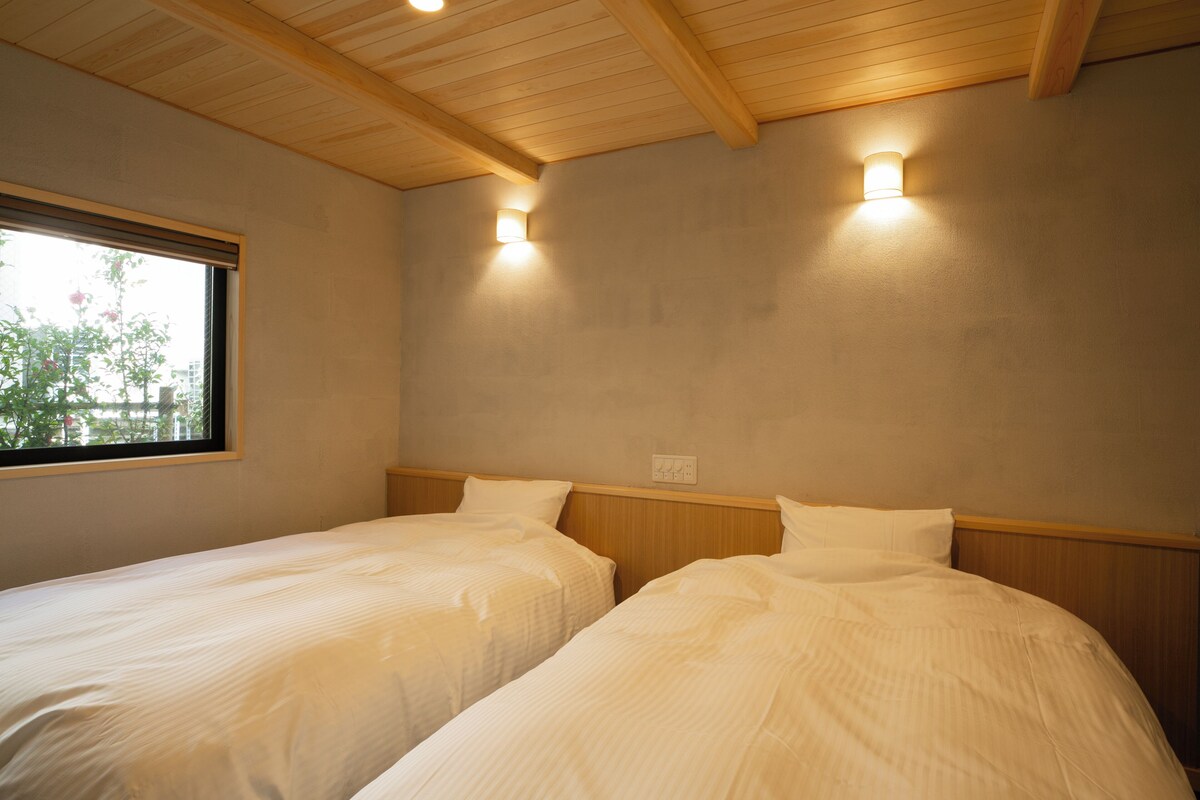 Quarto com duas camas, vigas de madeira no teto e duas luzes fixadas na parede.