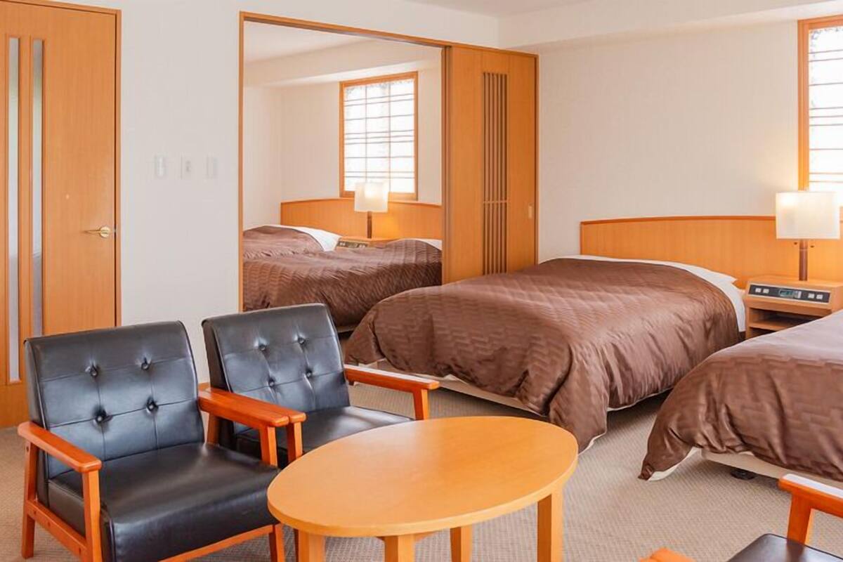 A hotel room with two beds, a seating area with chairs, a table, and a large mirror.