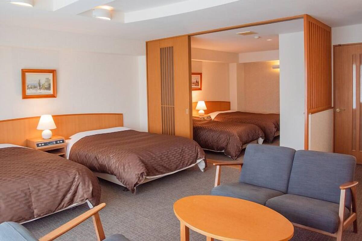 A hotel room with two beds, a sofa, a small table, and a mirror.