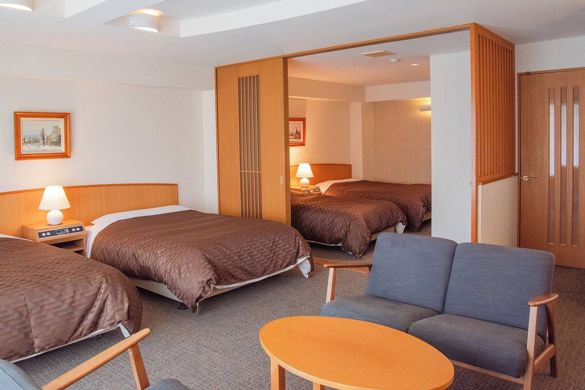 A hotel room with two beds, a sofa, a small table, and a mirror.