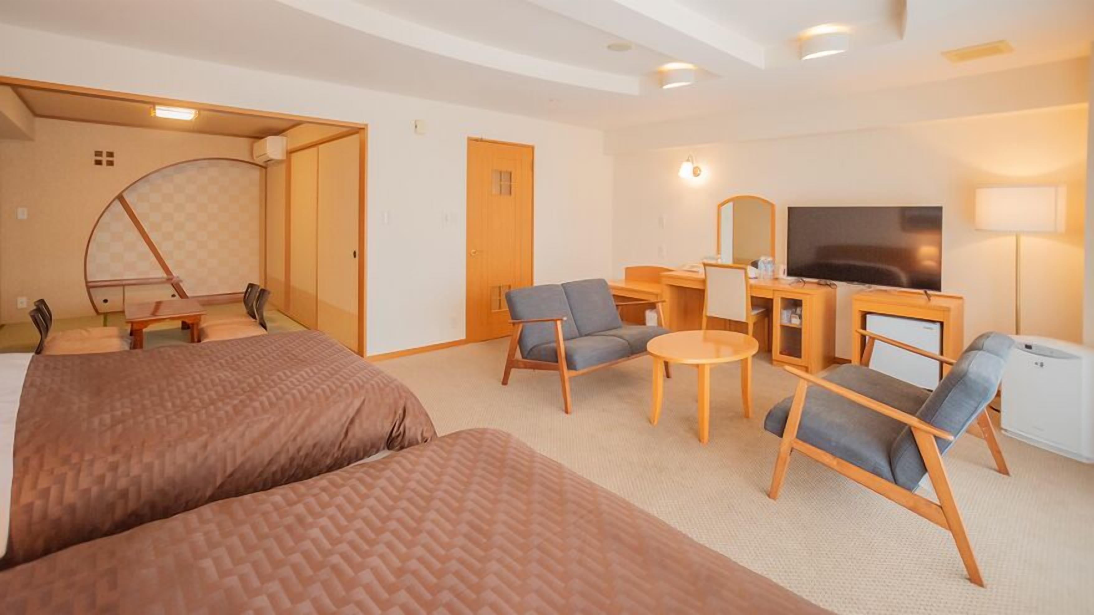 A hotel room with a bed, two armchairs, a desk with a TV, and a small table.
