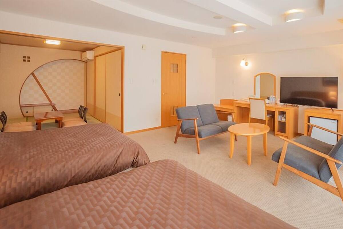 A hotel room with a bed, two armchairs, a desk with a TV, and a small table.