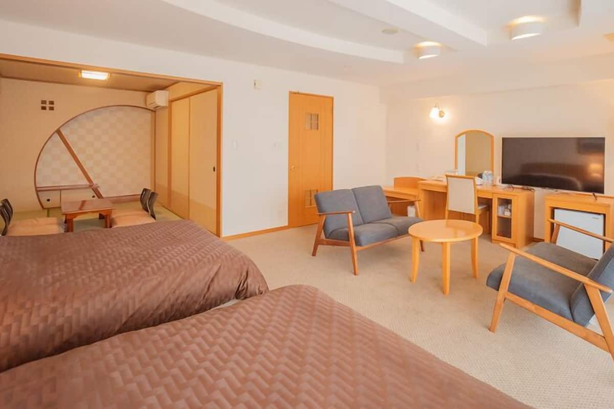 A hotel room with a bed, two armchairs, a desk with a TV, and a small table.